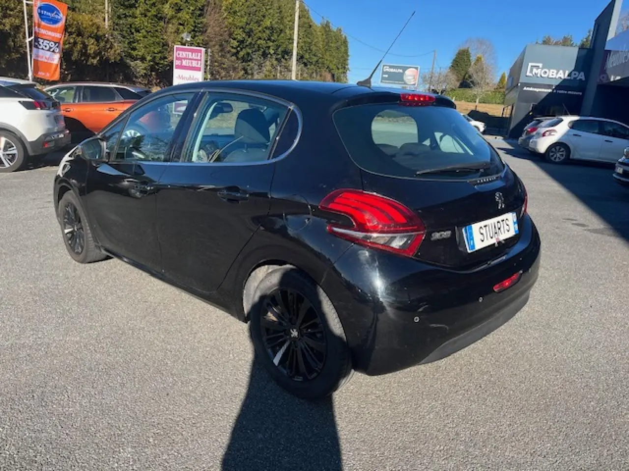 Peugeot 208 noire vue 3/4 arrière droit, avec feux arrière distinctifs et jantes noires, stationnée en extérieur.