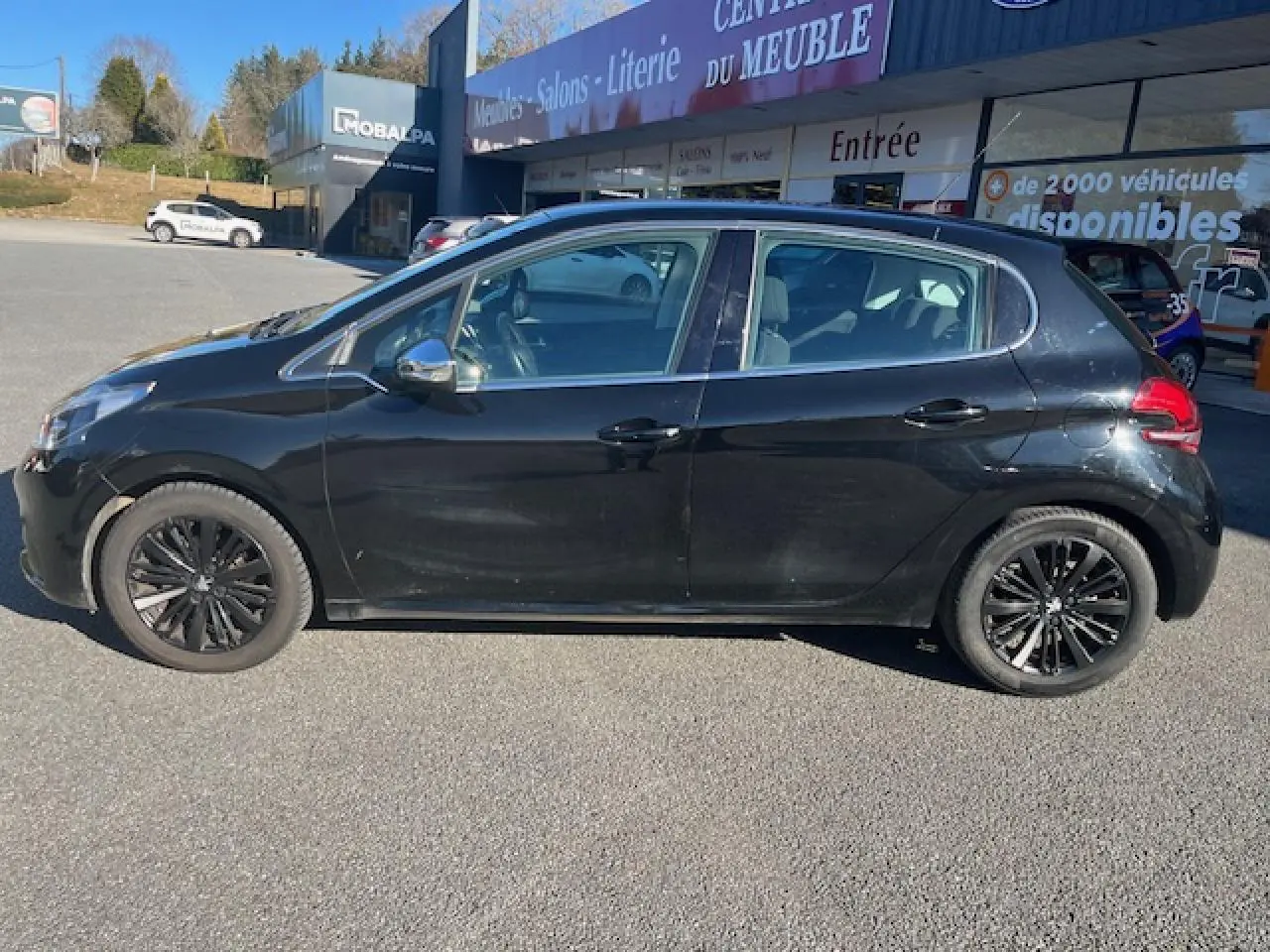 Profil côté gauche d'une Peugeot 208 noire de 2017, avec jantes noires et vitres légèrement teintées, stationnée en extérieur.