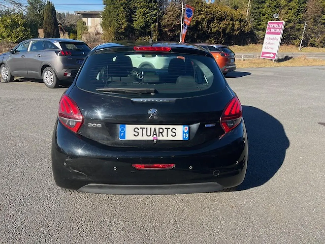 Vue arrière d'une Peugeot 208 noire 2017 avec radars de recul et plaque d'immatriculation visible en extérieur.