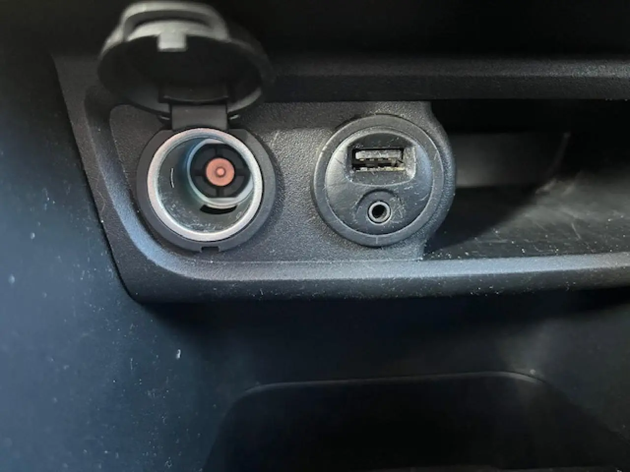 Prise 12V et port USB en gros plan sur la console centrale d'une Peugeot 208 noire de 2017.