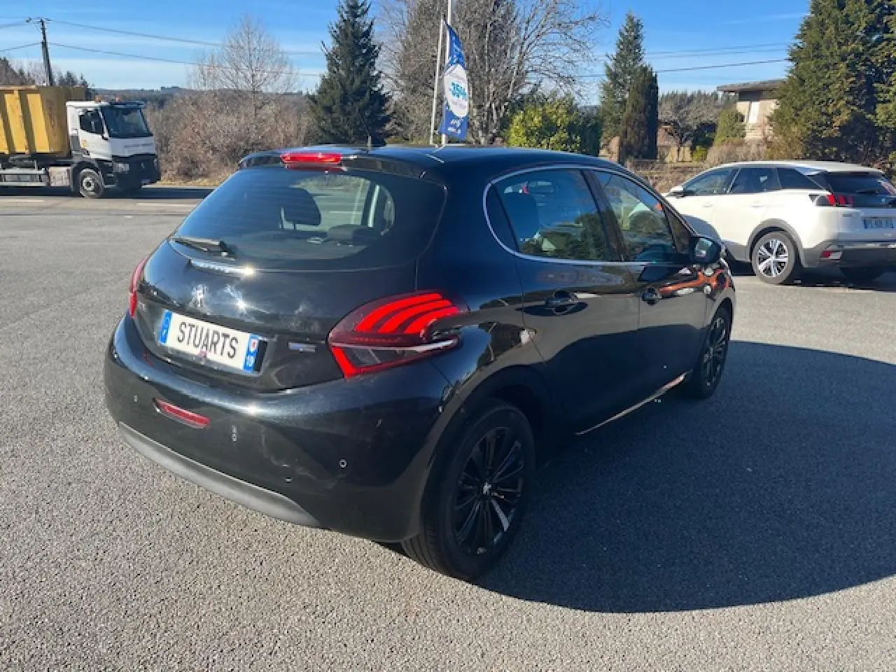 Peugeot 208 noire vue en 3/4 arrière droit, avec feux arrière distinctifs et jantes noires sur parking extérieur.