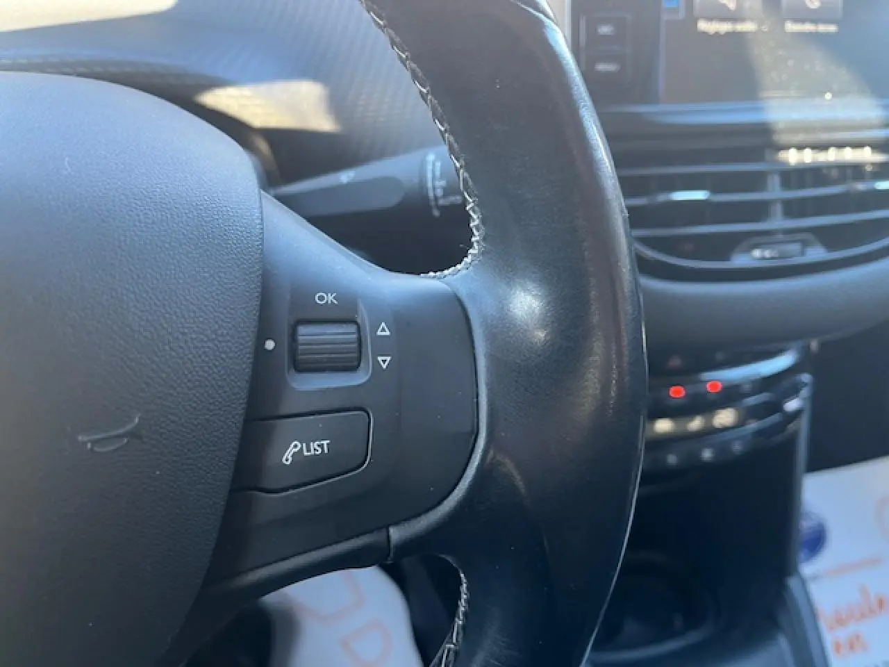 Gros plan sur le volant noir multifonction de la Peugeot 208 2017 avec commandes intégrées et tableau de bord flou en arrière-plan.