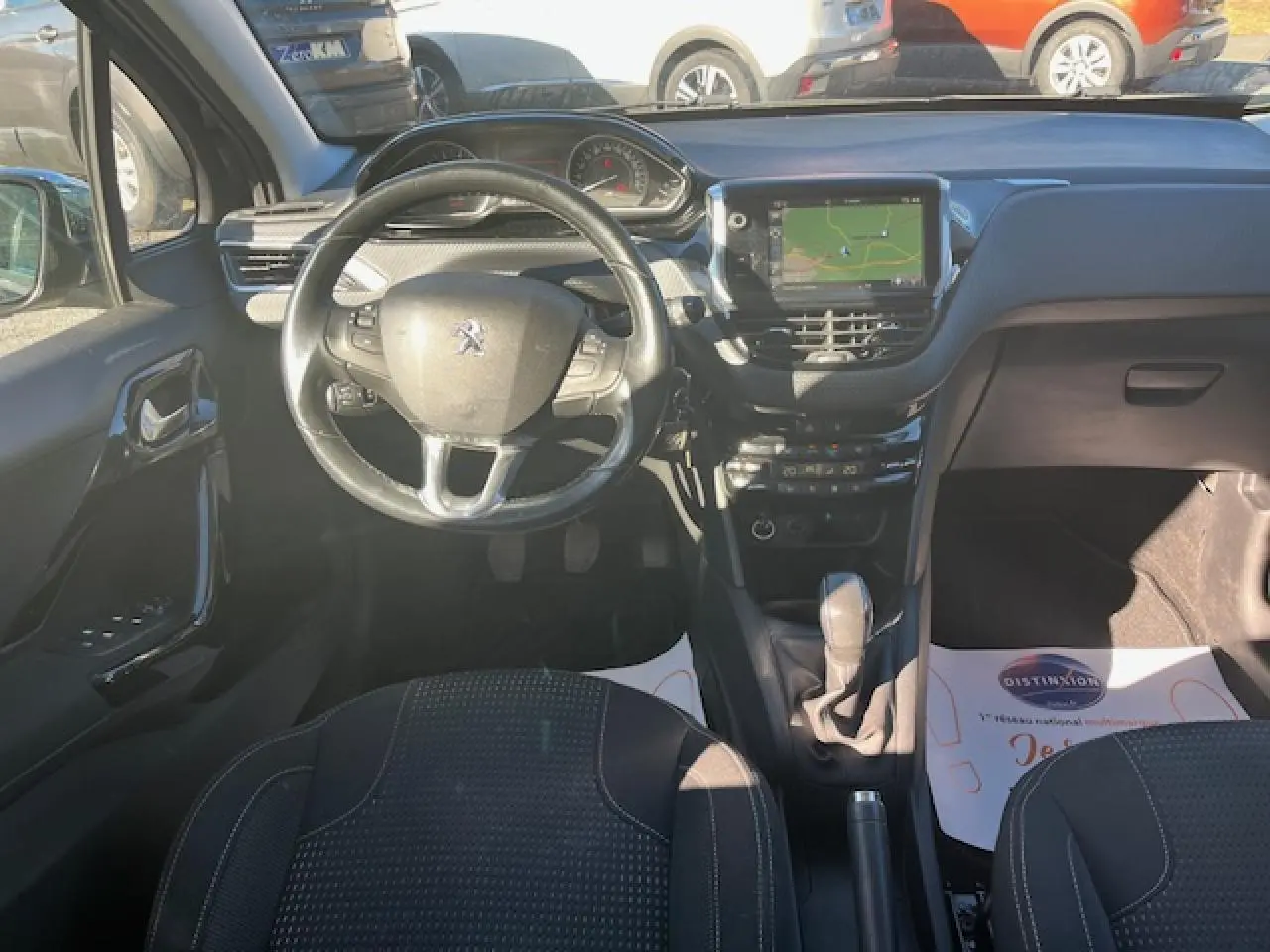 Vue intérieure avant de la Peugeot 208 noire, montrant le volant multifonction, écran tactile et levier de vitesse manuel.