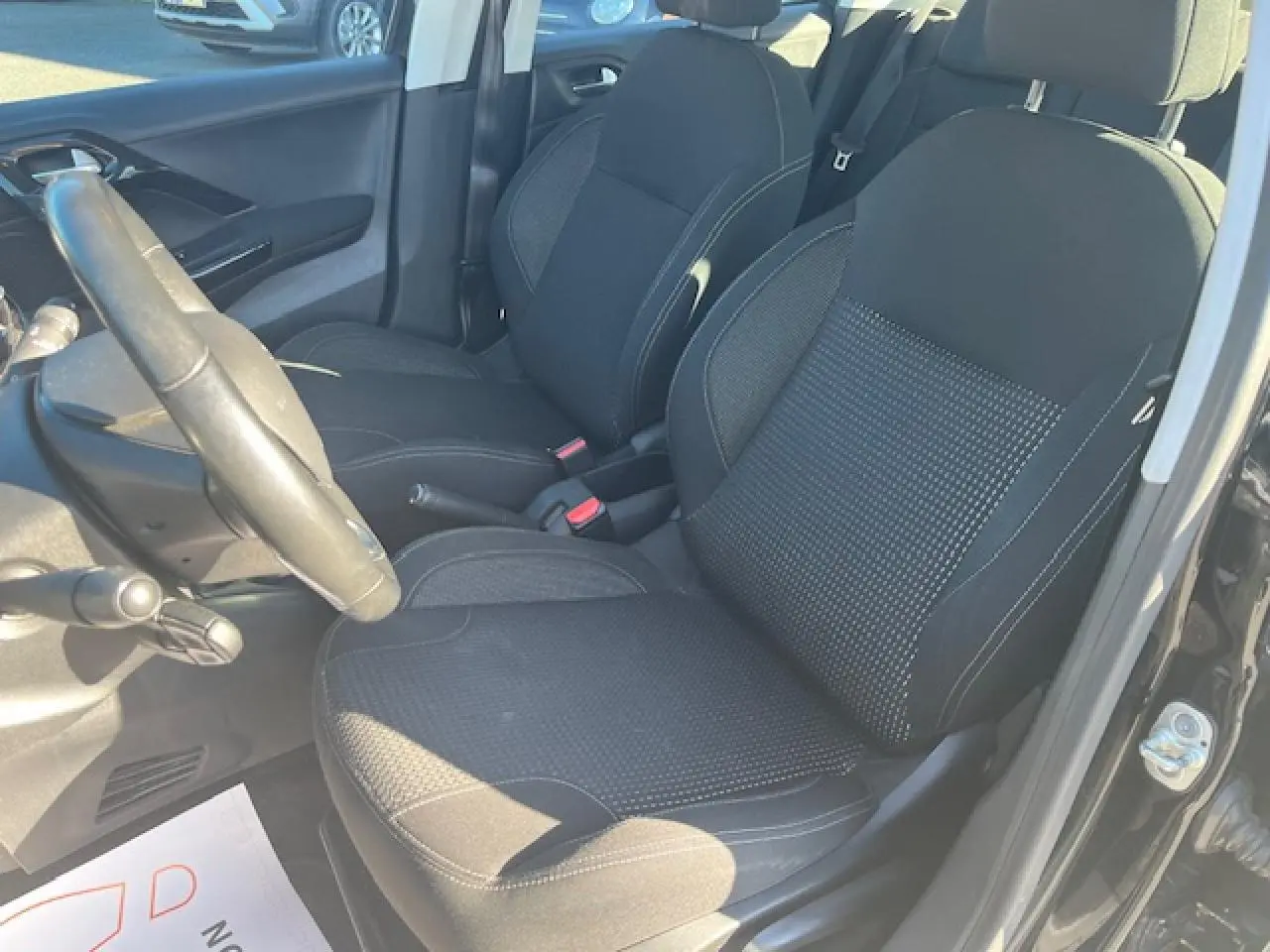 Vue intérieure côté conducteur de la Peugeot 208 noire, montrant les sièges avant en tissu et le volant multifonction.