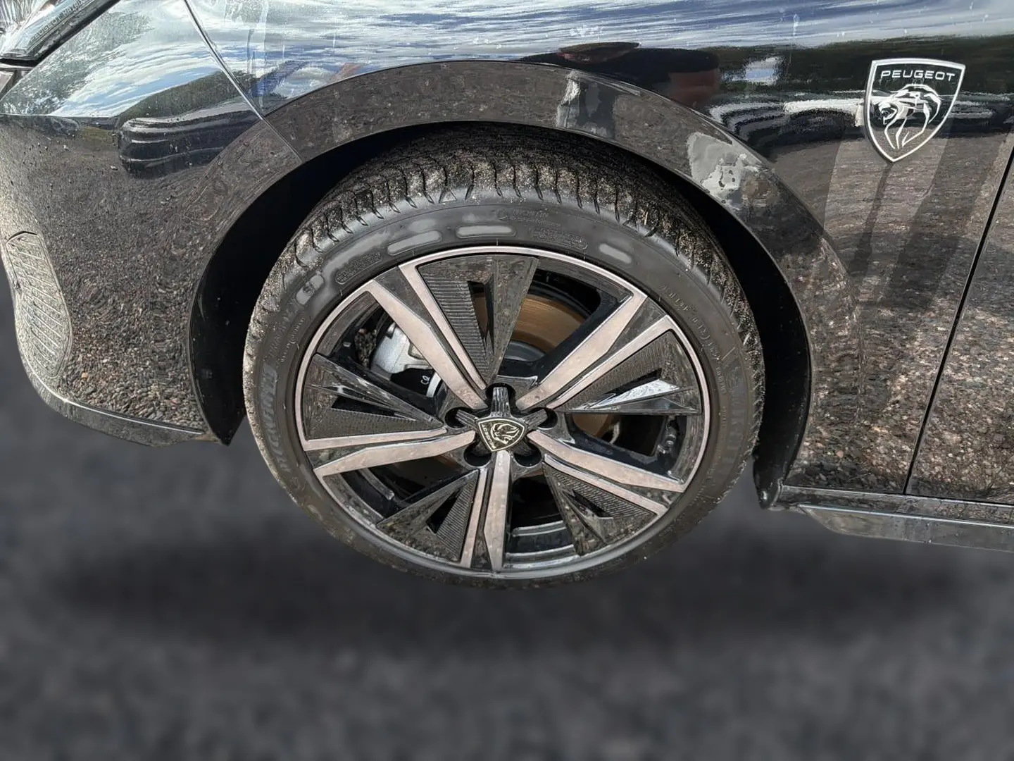 Gros plan sur la roue avant droite noire d'une Peugeot 308 1.2 hybrid 145 GT avec jante alu au design moderne et logo Peugeot visible.