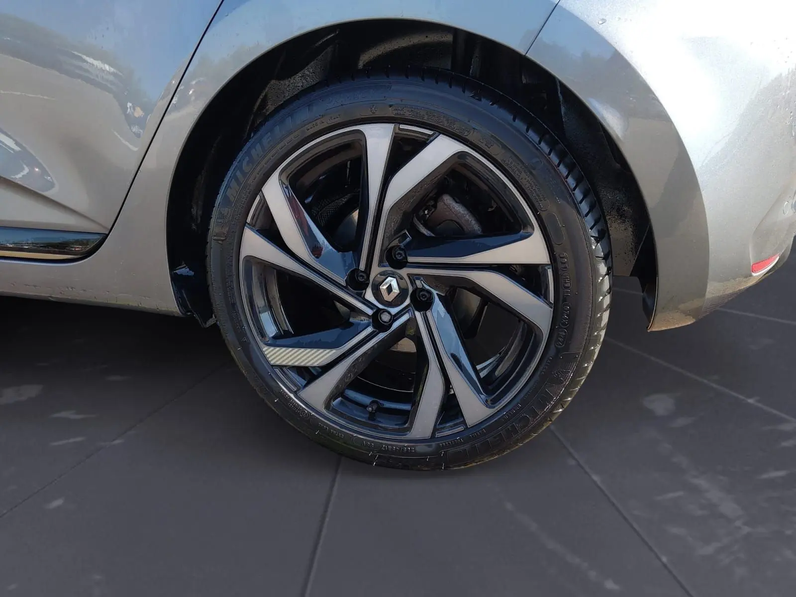 Gros plan sur la roue arrière droite d’une Renault Clio V gris foncé métal avec jante alliage noire et argentée.