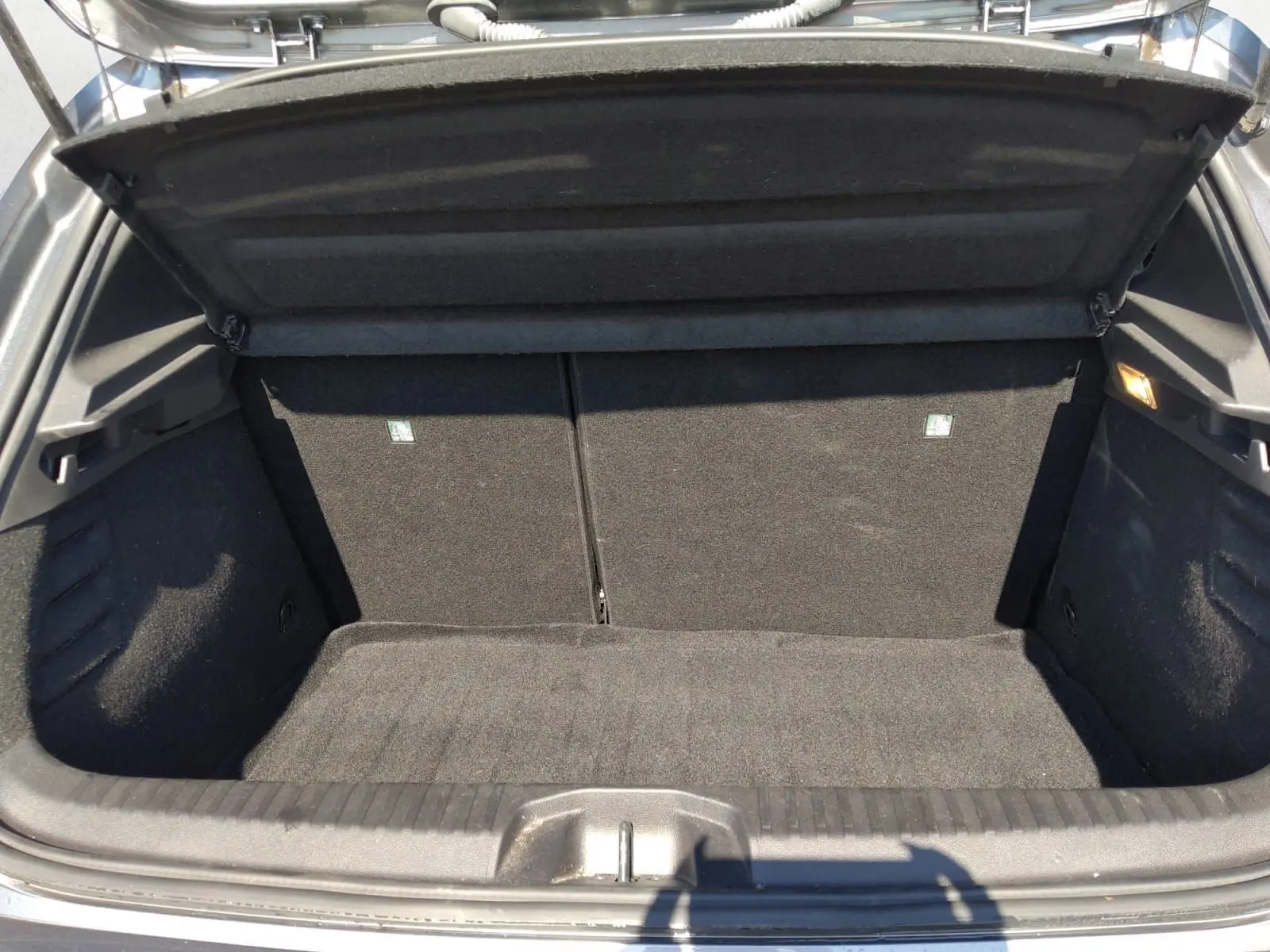 Coffre ouvert vu de face d'une Renault Clio V E-Tech Full Hybrid gris foncé métal, intérieur noir et tapis de coffre propre.
