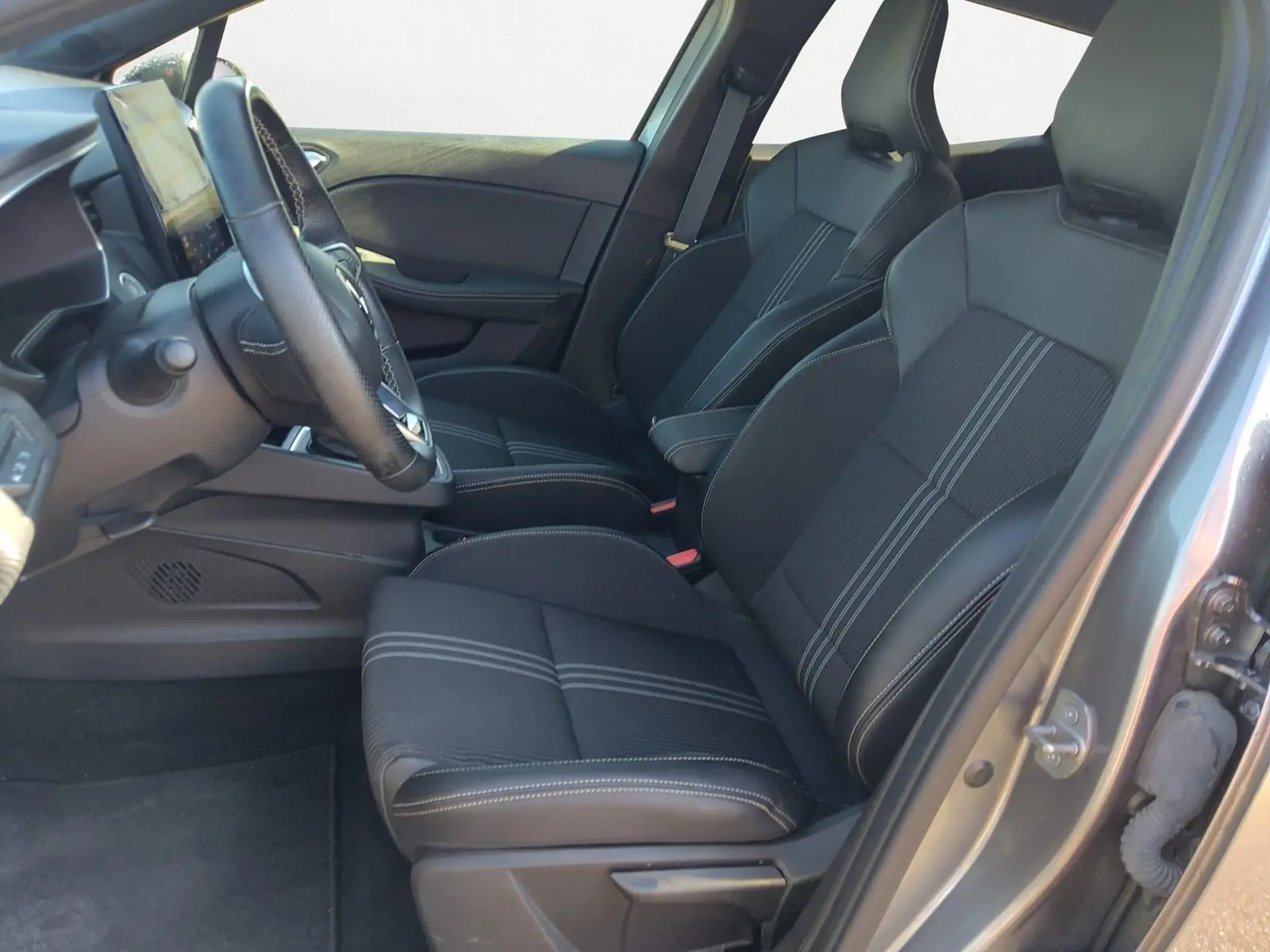 Vue intérieure côté conducteur de la Renault Clio V E-Tech hybride 2023, sièges noirs avec surpiqûres blanches.