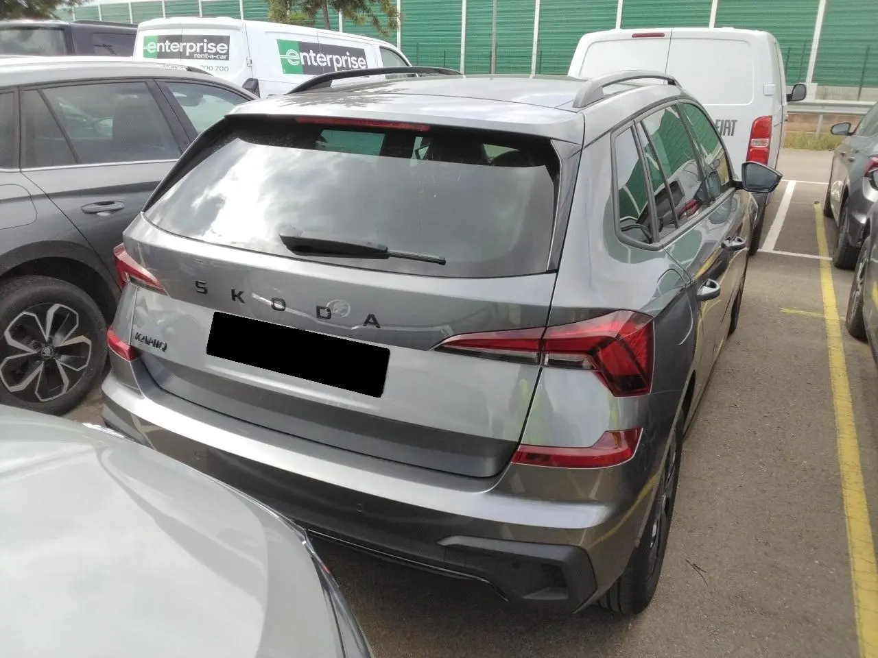 Vue 3/4 arrière d'un Skoda Kamiq gris graphite avec hayon électrique et toit panoramique visible en stationnement.
