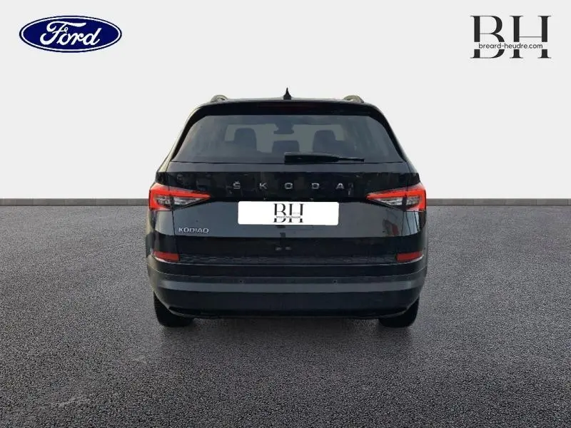Vue arrière d'un Skoda Kodiaq noir Magic Nacré avec hayon ouvert et feux arrière LED visibles sur un sol gris.