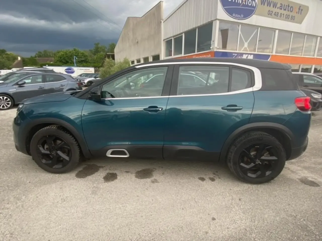 Vue latérale gauche d'un Citroën C5 Aircross bleu Tijuca avec toit noir et jantes alliage noires, stationné en extérieur.