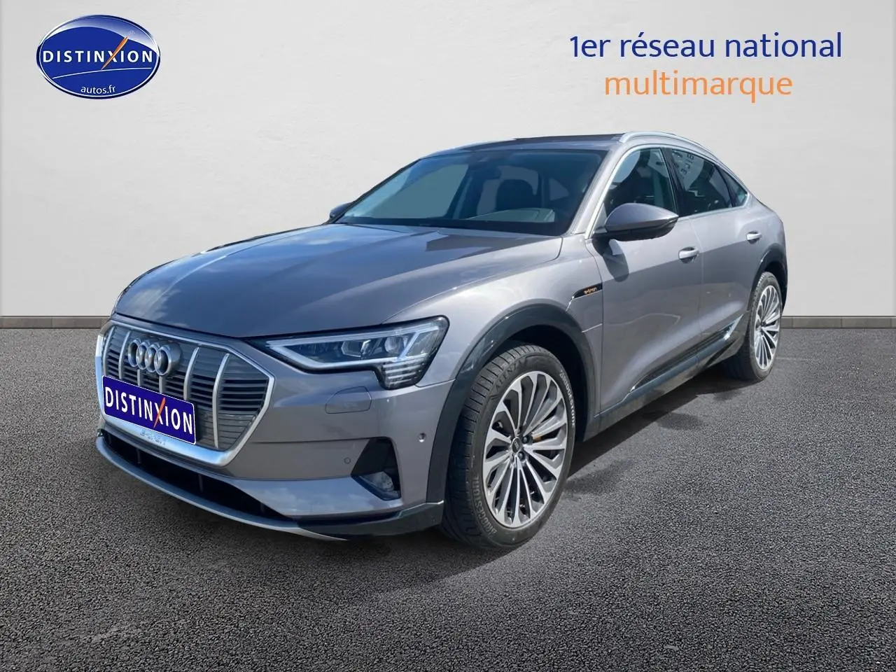 Audi Q8 E-TRON gris en 3/4 avant droit, avec calandre distinctive et jantes alu multibranches visibles.