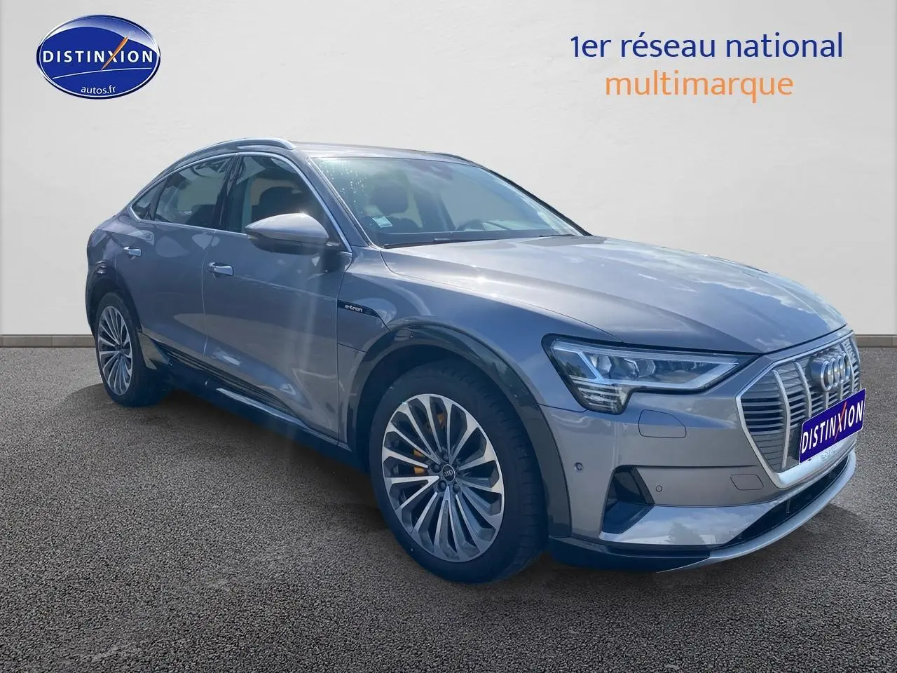 Audi Q8 E-Tron gris en 3/4 avant droit, mettant en valeur sa calandre distinctive et ses jantes alu élégantes.