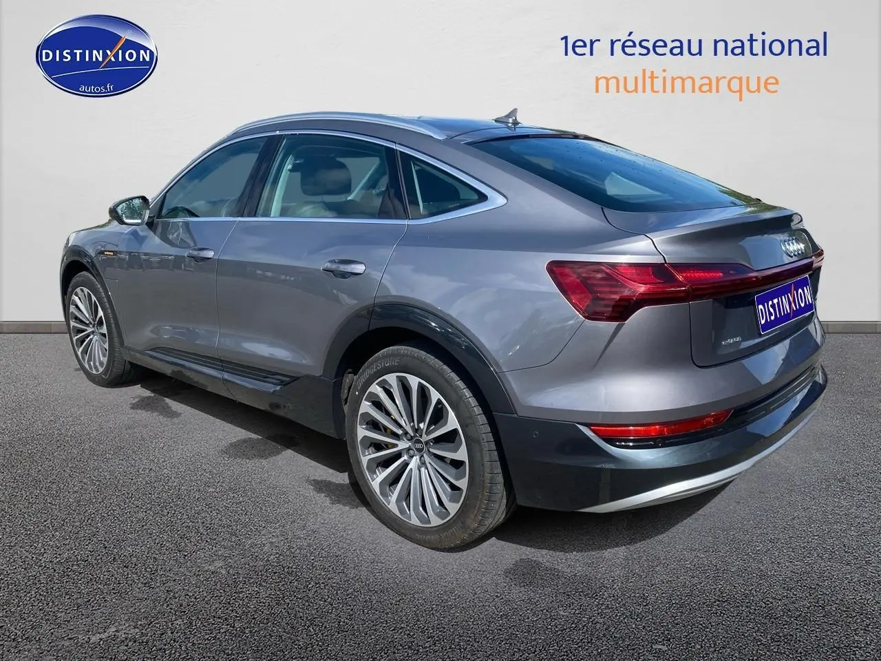 Audi Q8 E-TRON gris vu en 3/4 arrière côté gauche, soulignant ses jantes alu et feux arrière LED.