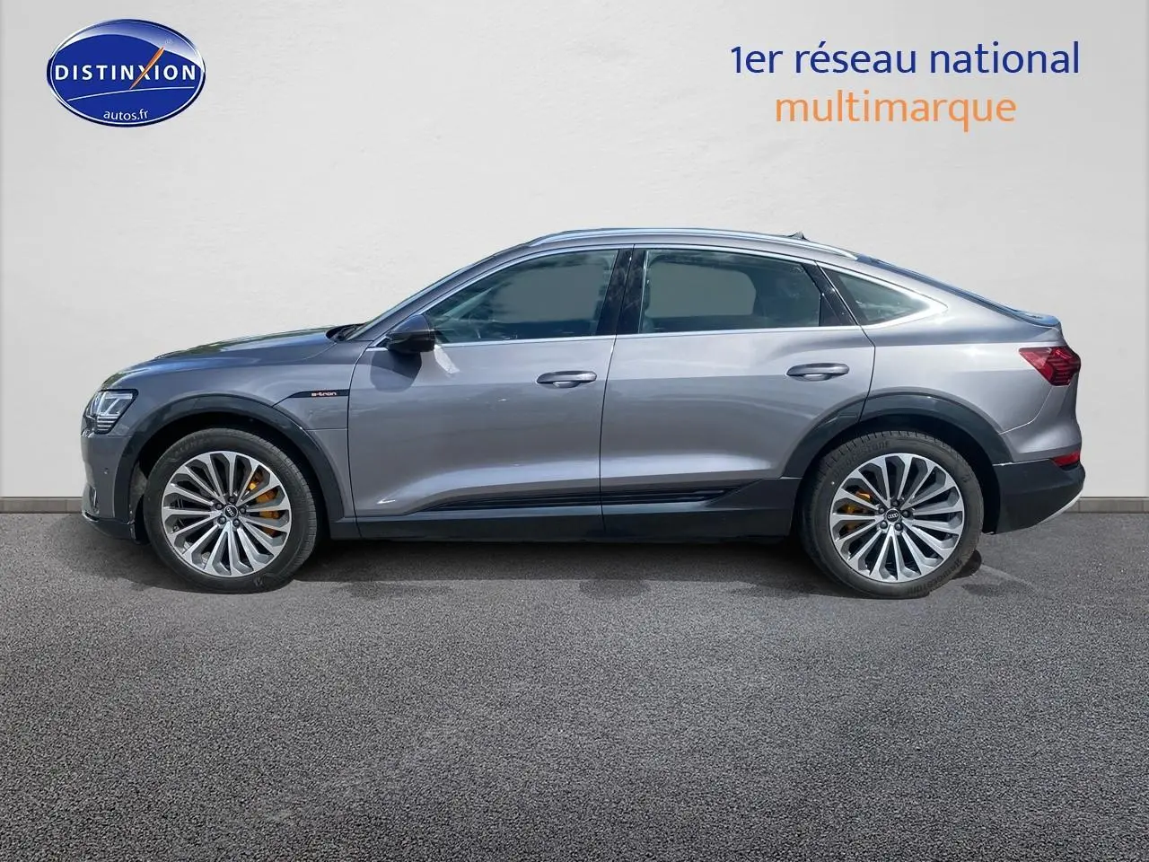 Audi Q8 E-Tron gris en vue profil côté gauche, avec jantes alu et étriers de frein orange visibles.