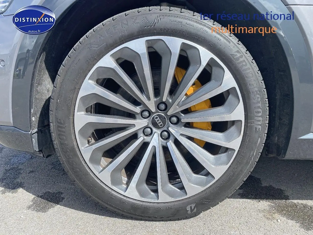 Gros plan sur la jante alu grise avec logo Audi et étrier de frein jaune du côté avant gauche du Q8 E-TRON gris.