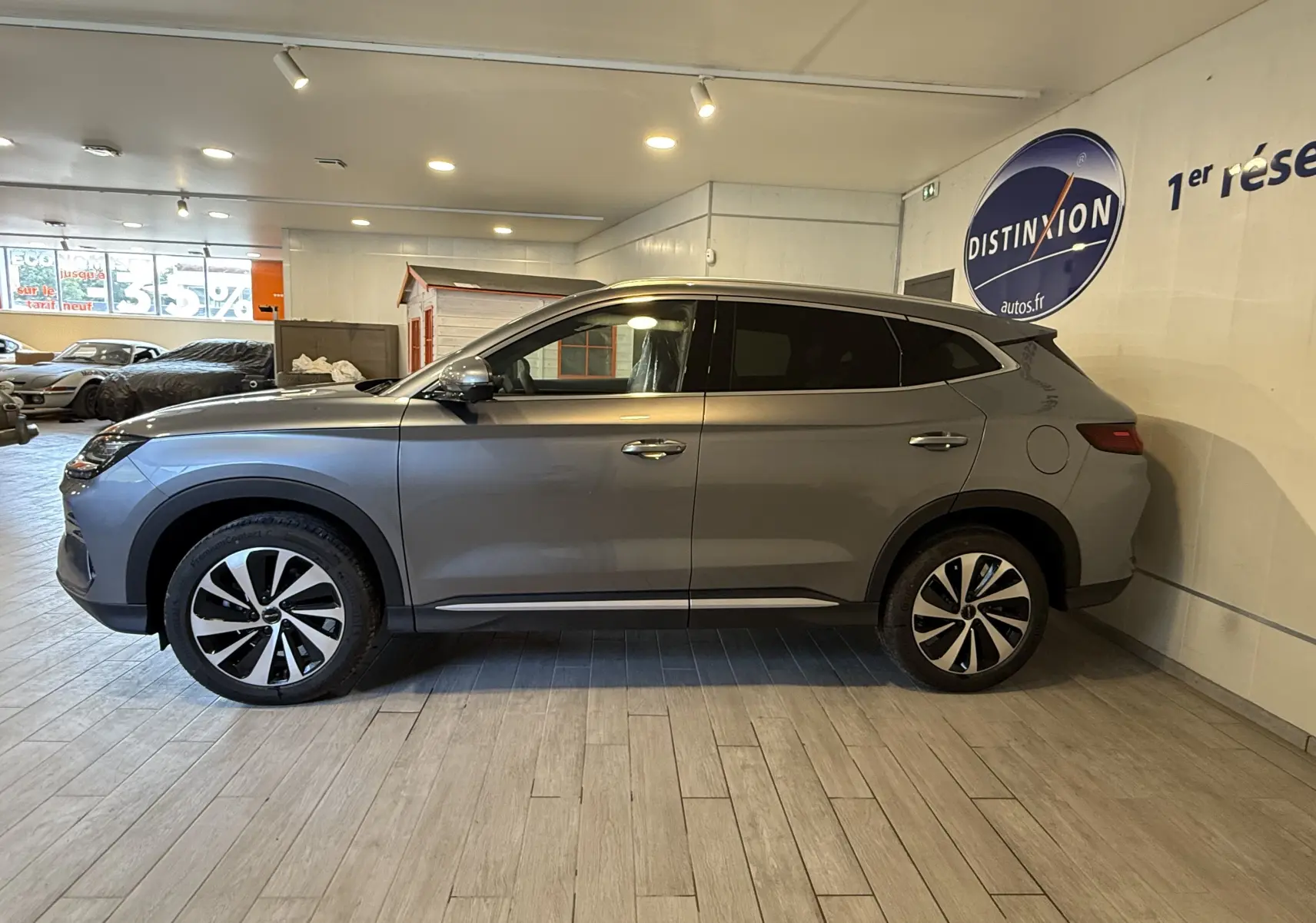 Vue latérale droite du SUV BYD SEAL U gris, hybride rechargeable, avec jantes bicolores et vitres teintées, en intérieur showroom.