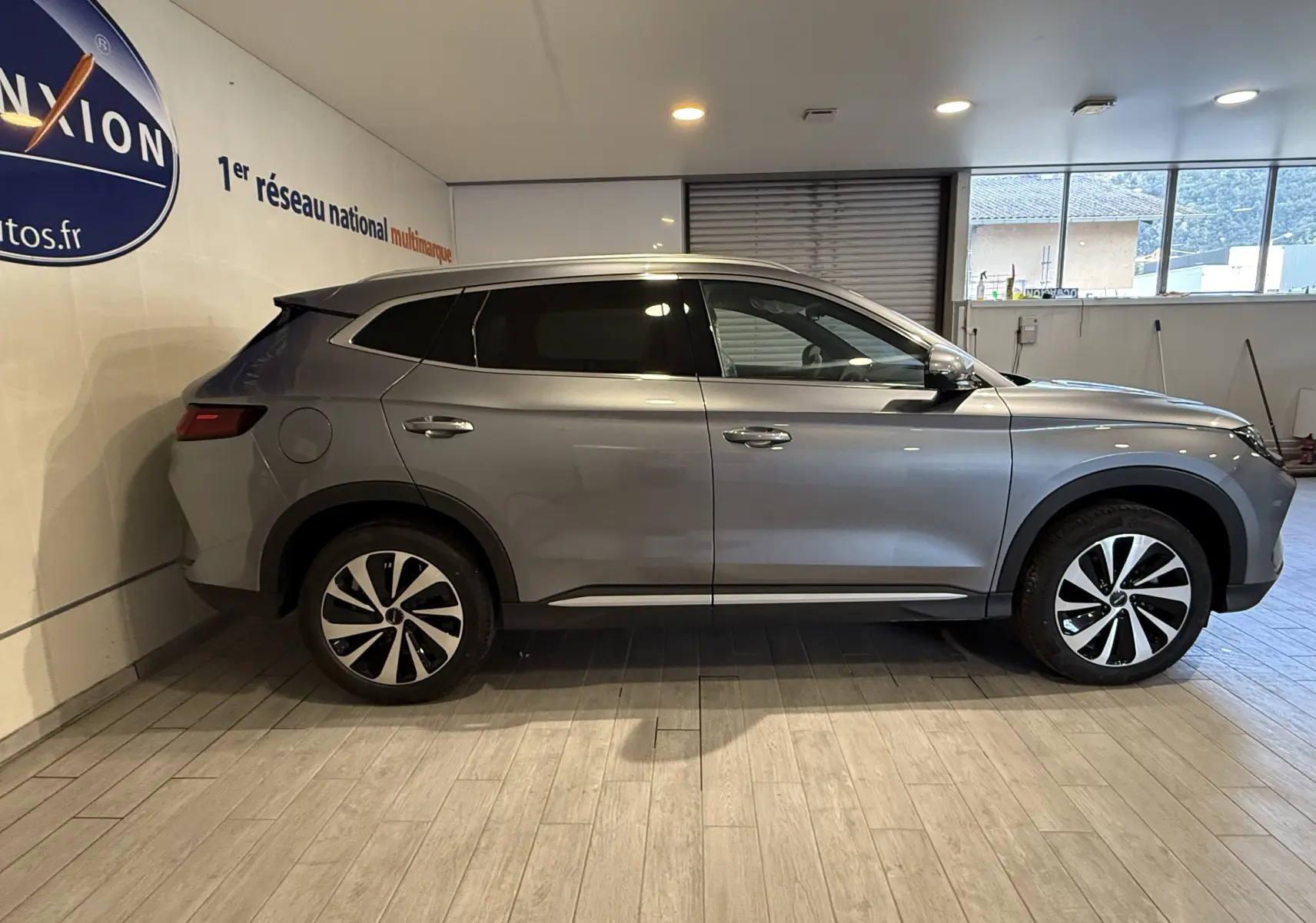 Vue de profil côté gauche du SUV BYD SEAL U gris, hybride rechargeable, garé en intérieur avec jantes bicolores distinctives.