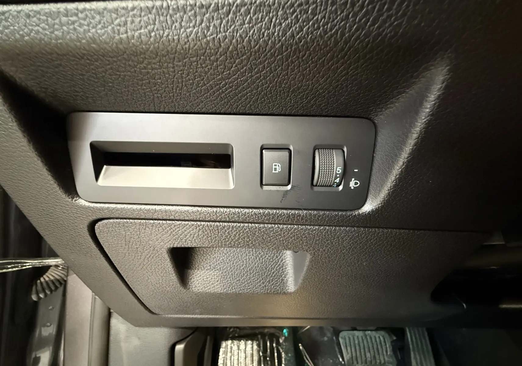 Détail intérieur côté gauche montrant les commandes d’ouverture du réservoir et de réglage des phares sur plastique noir texturé.