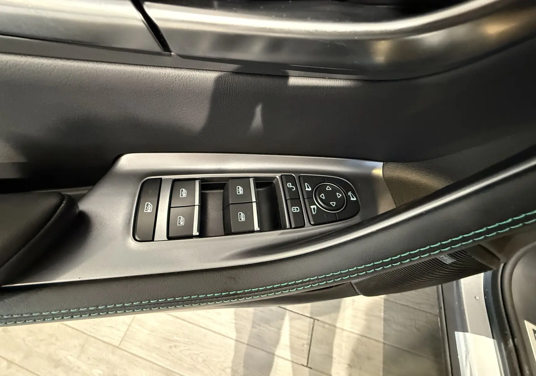 Gros plan sur les commandes des vitres et rétroviseurs sur la porte côté gauche du BYD SEAL U gris, avec surpiqûres vertes.
