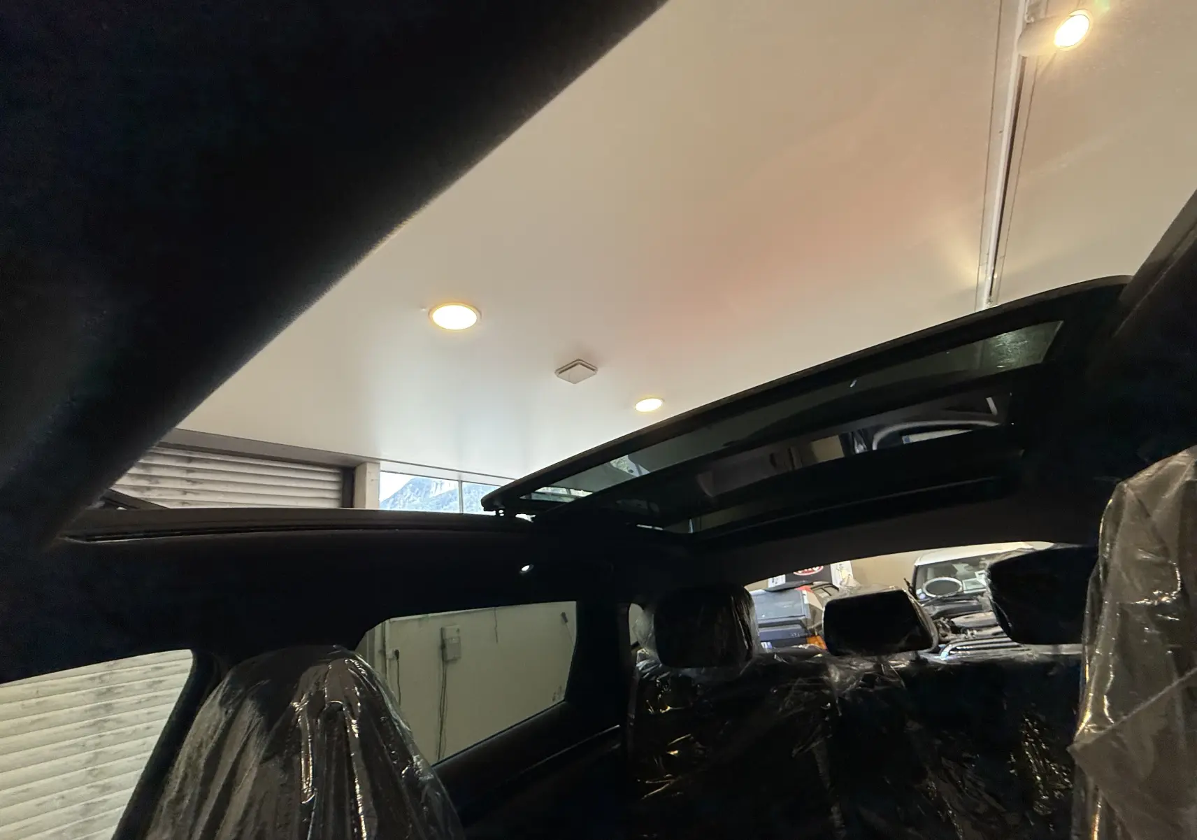 Vue intérieure du toit ouvrant panoramique du BYD SEAL U gris, avec sièges arrière protégés par des housses plastiques.