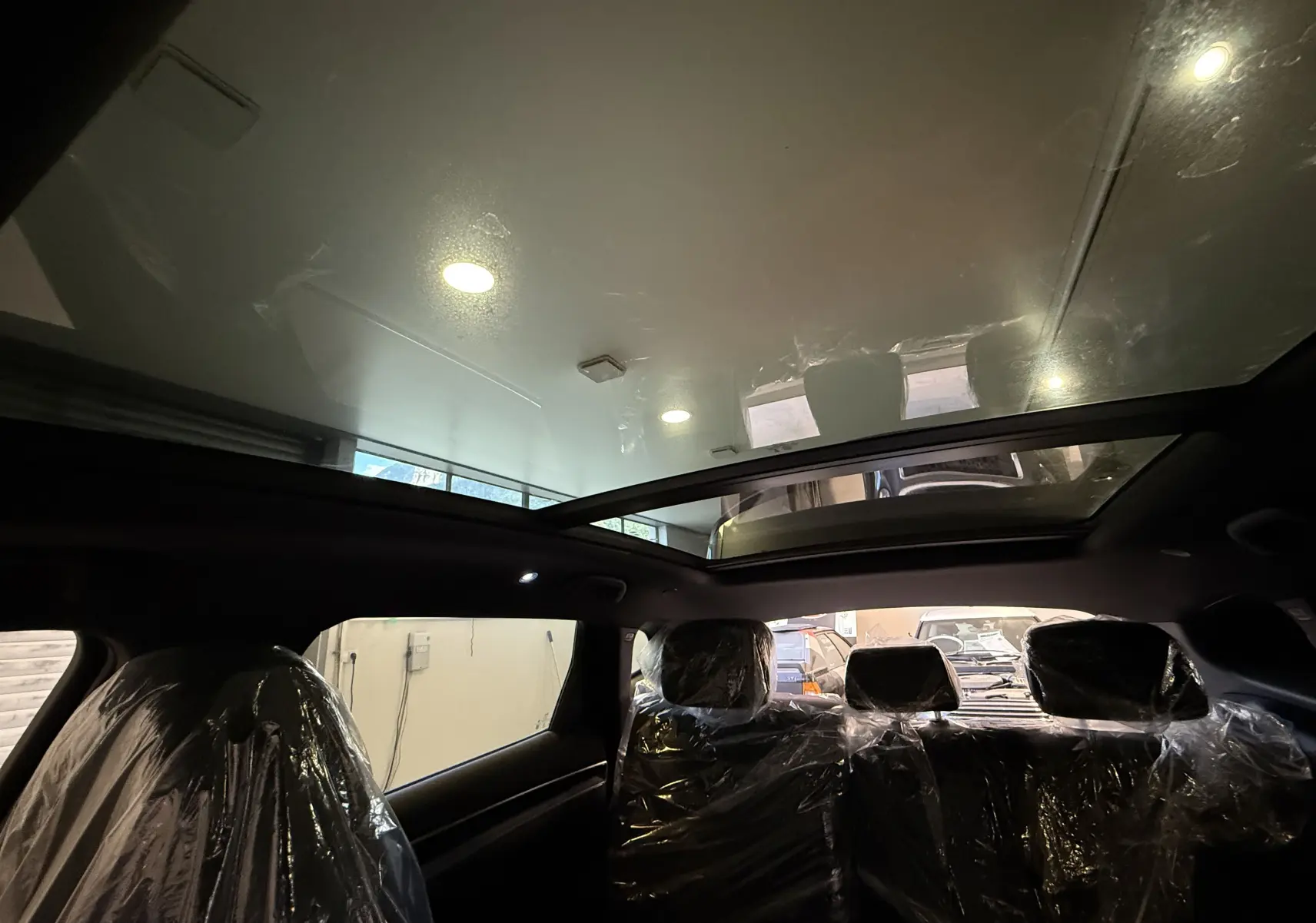 Vue intérieure du toit panoramique en verre du BYD SEAL U gris, avec sièges arrière protégés par des housses plastiques.