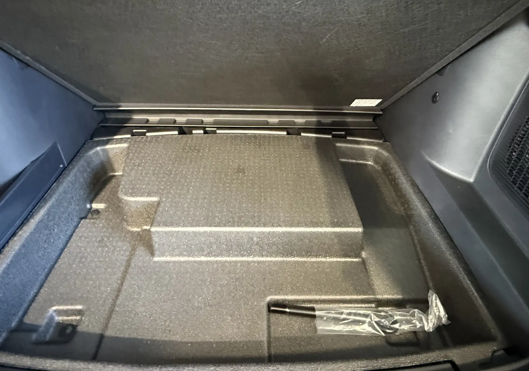 Coffre ouvert en vue plongeante montrant un espace de rangement vide avec un outil emballé dans un BYD SEAL U gris.