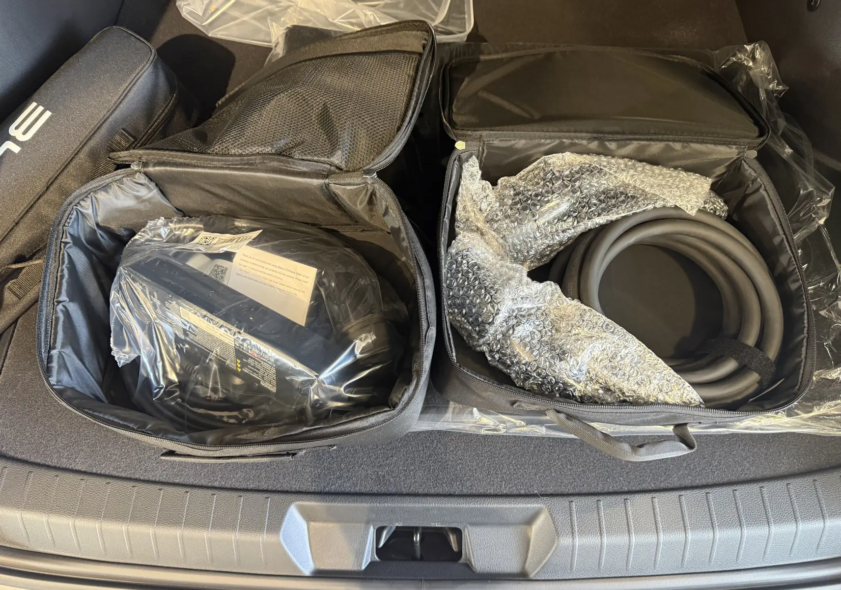 Vue plongeante sur le coffre gris du BYD SEAL U avec deux sacs ouverts contenant câbles de recharge et accessoires.