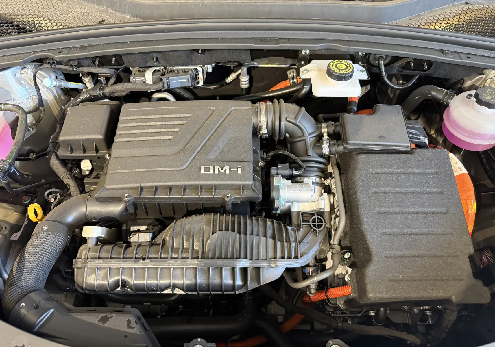 Vue plongeante sur le moteur hybride rechargeable gris du BYD SEAL U 1.5l DM-i avec détails des composants et câbles orange.