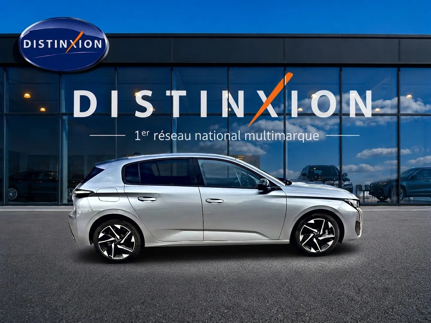Profil droit de la Peugeot 308 1.2 hybrid 145 allure e-dcs6 gris artense avec jantes alliage modernes devant un bâtiment Distinxion.