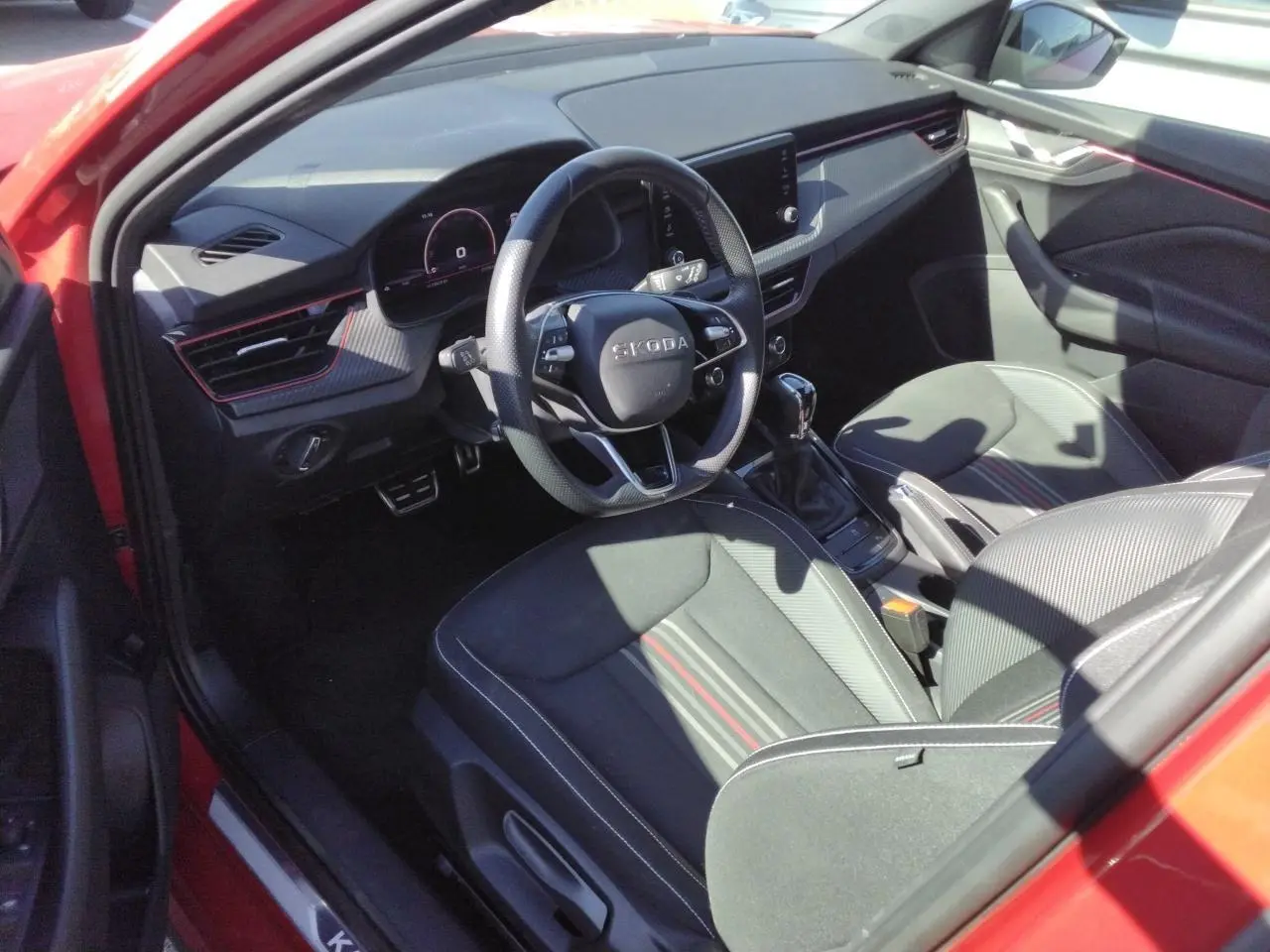 Intérieur côté conducteur du Skoda Kamiq Rouge Velvet, volant sport cuir, inserts carbone et sièges tissu noir à bandes rouges.