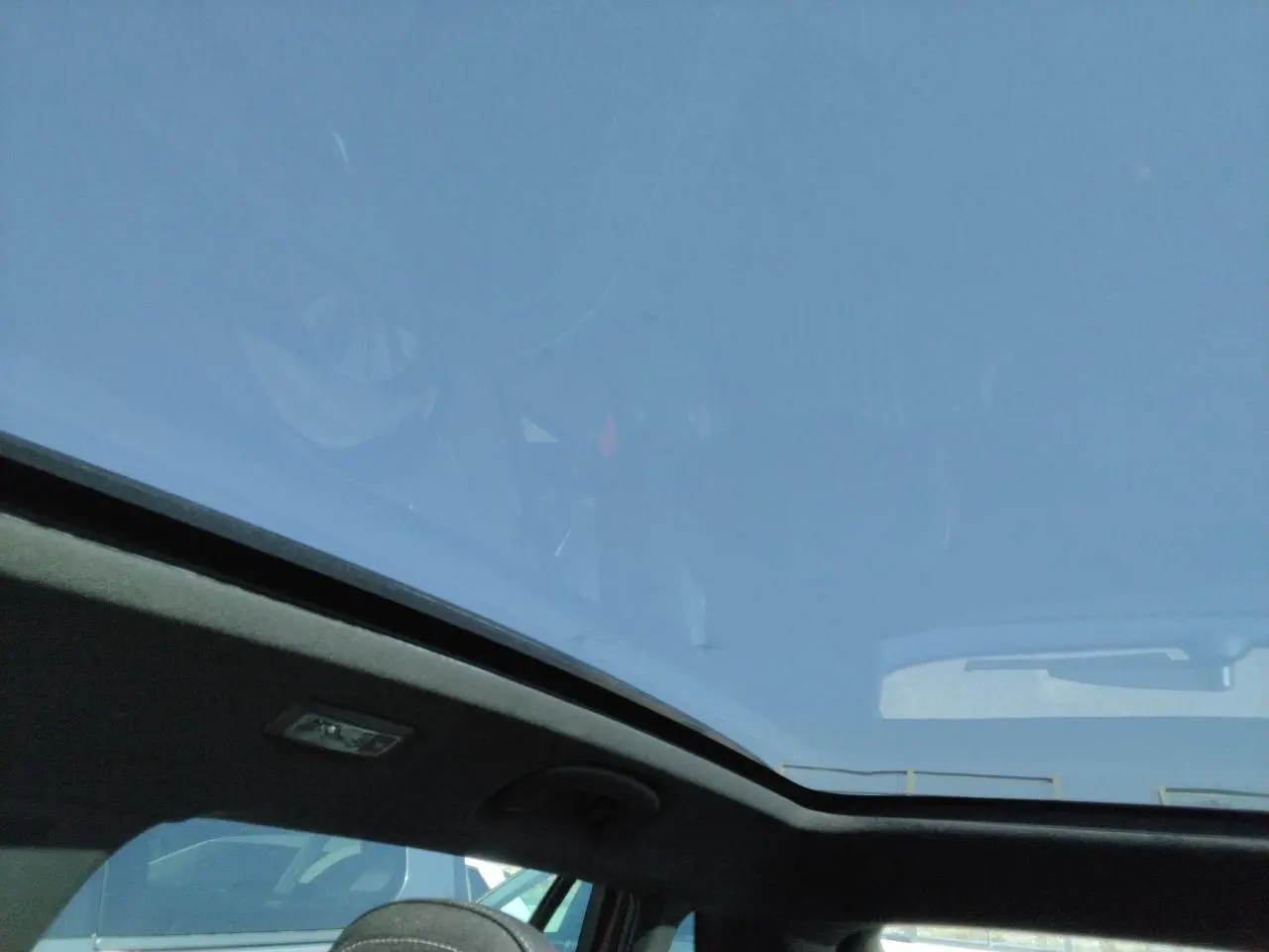 Vue intérieure montrant le toit panoramique noir du Skoda Kamiq Rouge Velvet avec ciel bleu visible à travers le verre.