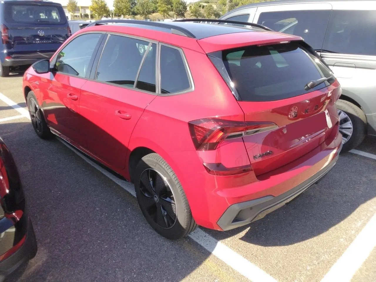 Vue 3/4 arrière droite d’un Skoda Kamiq rouge Velvet avec jantes noires et toit panoramique, stationné en extérieur.