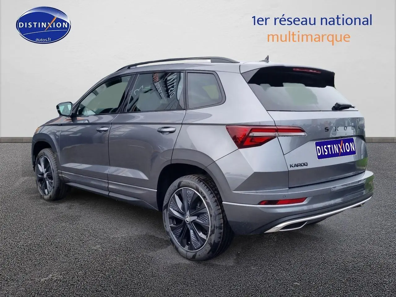Vue 3/4 arrière droite d'un SKODA KAROQ gris graphite avec jantes alu et barres de toit visibles.