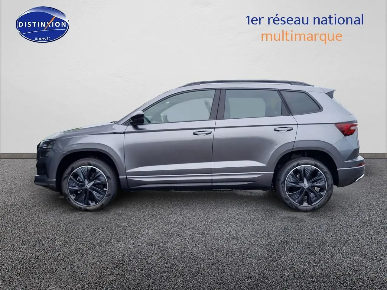 Profil côté gauche d'un SUV SKODA KAROQ gris graphite 2025 avec jantes alu et barres de toit visibles.