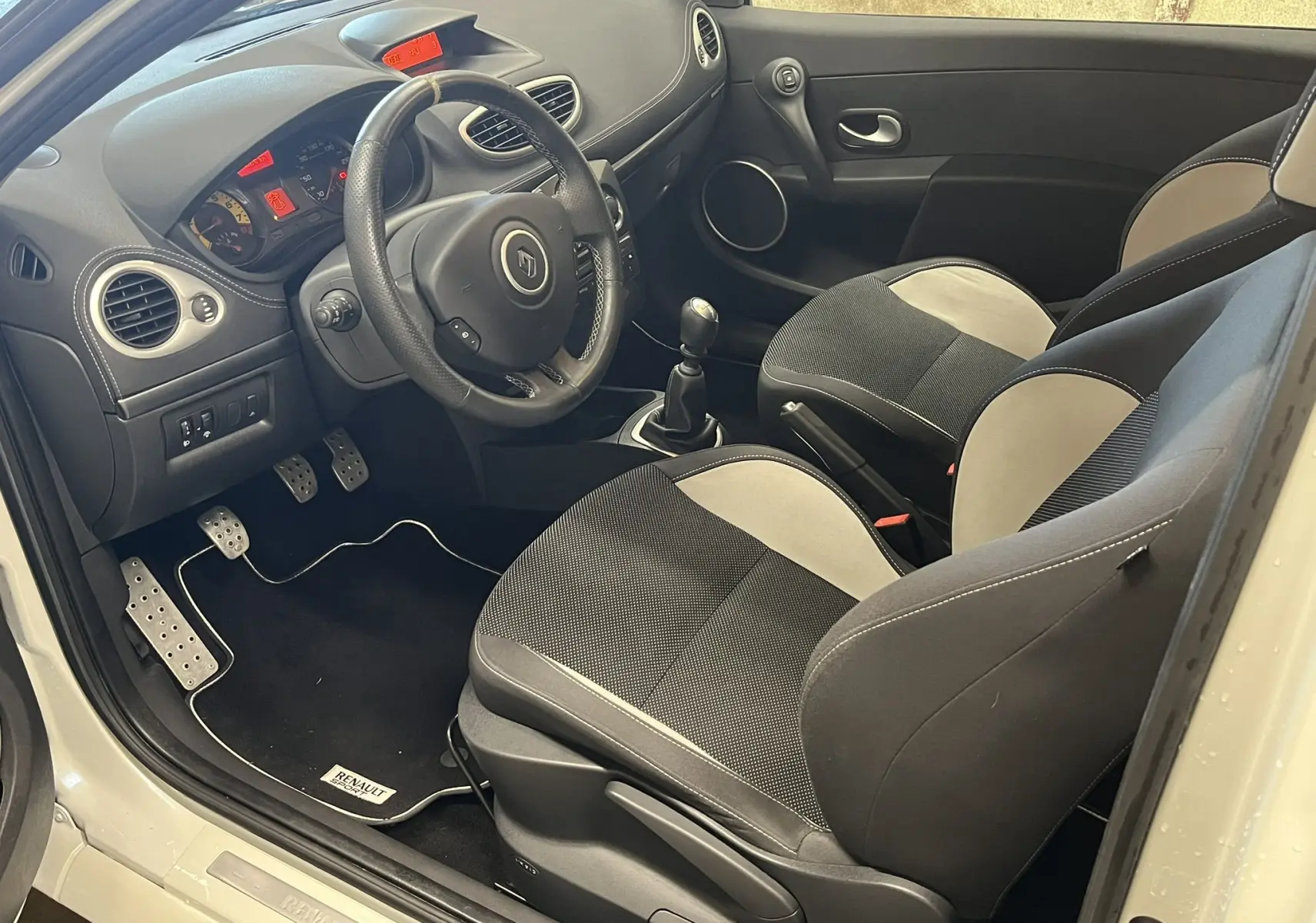 Vue intérieure côté conducteur de la Renault Clio III RS 20th Anniversary avec sièges bi-ton noir et beige et volant cuir.