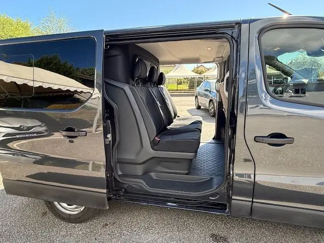 Vue latérale gauche du Renault Trafic gris comète avec porte coulissante ouverte, montrant les sièges arrière en rangée.