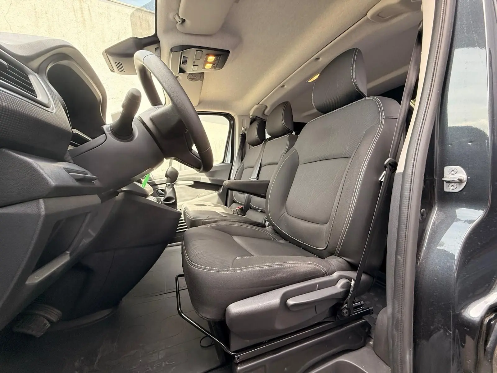 Vue intérieure côté conducteur du Renault Trafic gris comète 2024, montrant les sièges avant en tissu noir et le volant.