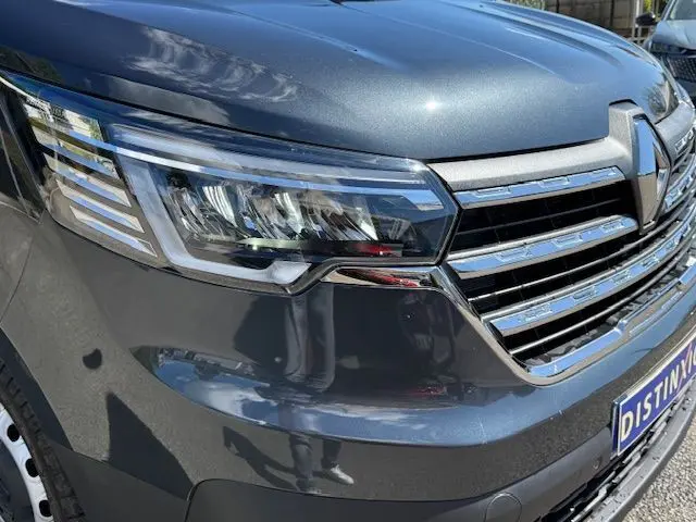 Gros plan sur l'avant droit gris comète du Renault Trafic 2024, mettant en valeur le phare et la calandre chromée.