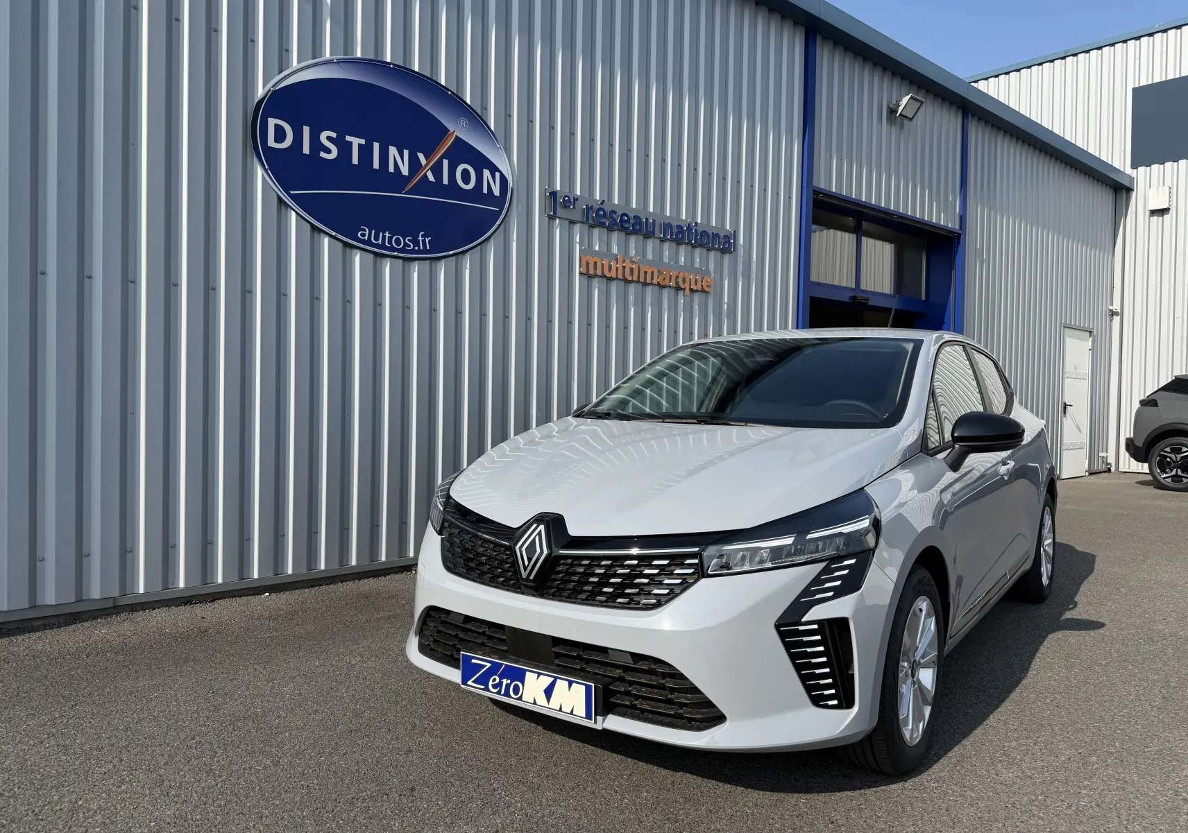 Vue 3/4 avant droite d'une Renault Clio 2025 gris rafale métal avec calandre noire et feux LED distinctifs.