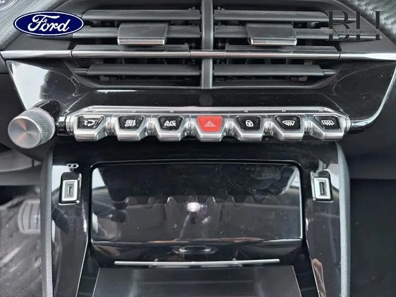 Vue rapprochée du tableau de bord noir brillant du Peugeot 2008 2021 avec boutons chromés et aérateurs horizontaux.