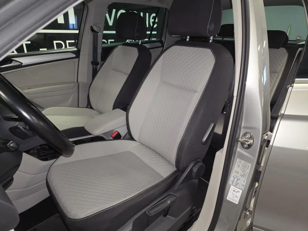 Vue intérieure côté conducteur du Volkswagen Tiguan 2018, sièges tissu gris clair avec accoudoir central.