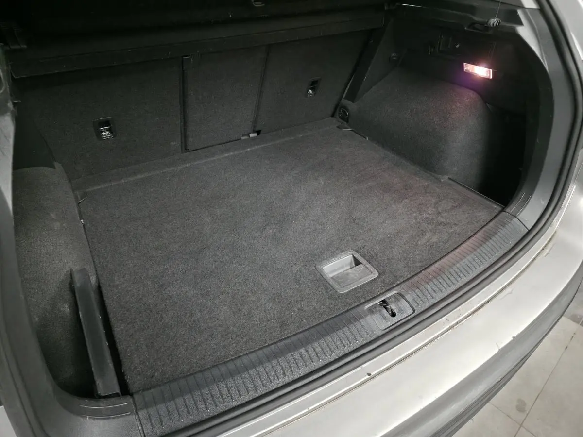 Coffre ouvert du Volkswagen Tiguan gris, vue plongeante montrant l'espace de chargement et l'éclairage intérieur.