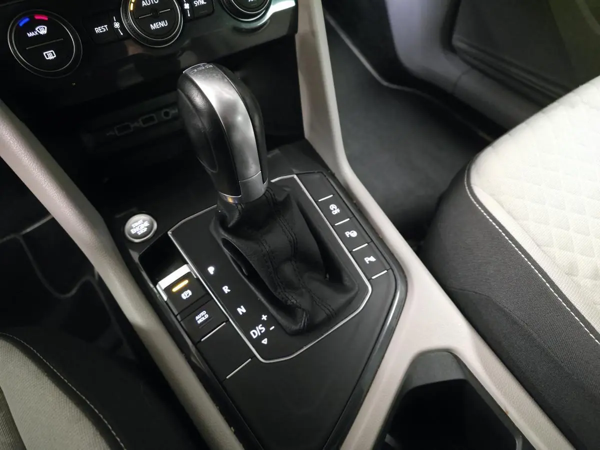 Gros plan sur le levier de vitesses automatique noir et cuir du Volkswagen Tiguan gris, avec console centrale et siège tissu clair.