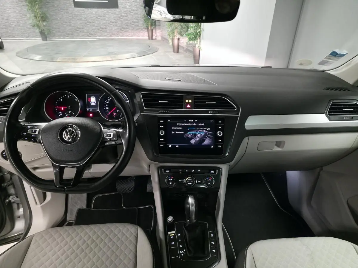 Vue intérieure avant du Volkswagen Tiguan gris, tableau de bord avec écran tactile et volant multifonctions cuir.
