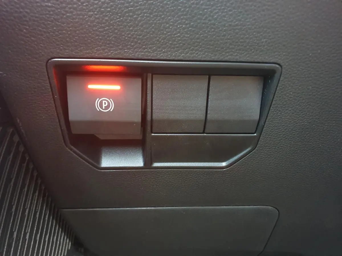 Gros plan sur le bouton de frein de stationnement électrique allumé, intérieur noir du Dacia Duster 1.6 Hybrid 2026.