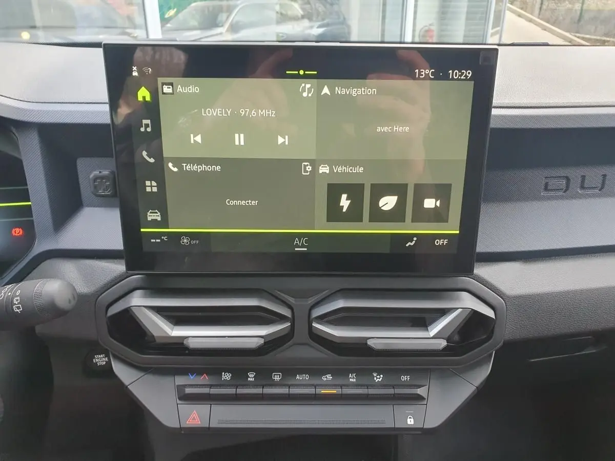 Vue rapprochée du tableau de bord du Dacia Duster 2026, écran tactile central avec commandes climatisation et aérateurs noirs.