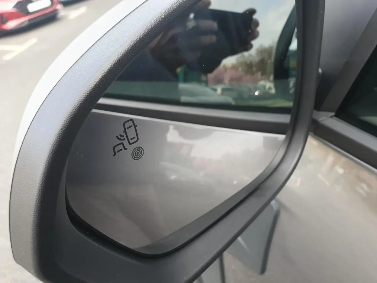 Rétroviseur extérieur côté gauche du Dacia Duster gris schiste 2026 avec indicateur d'angle mort visible.