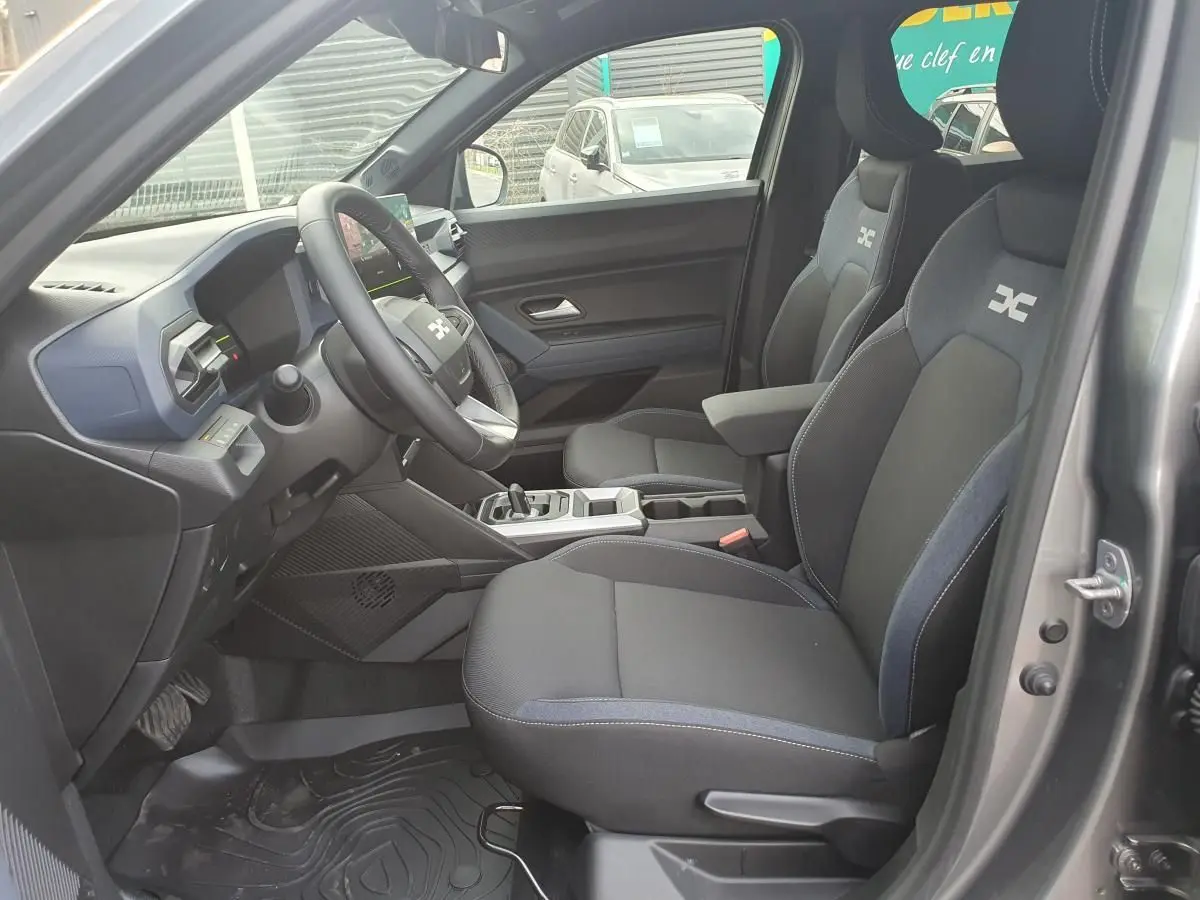 Vue intérieure côté conducteur du Dacia Duster 2026 gris schiste, sièges tissu avec logo et tableau de bord moderne.