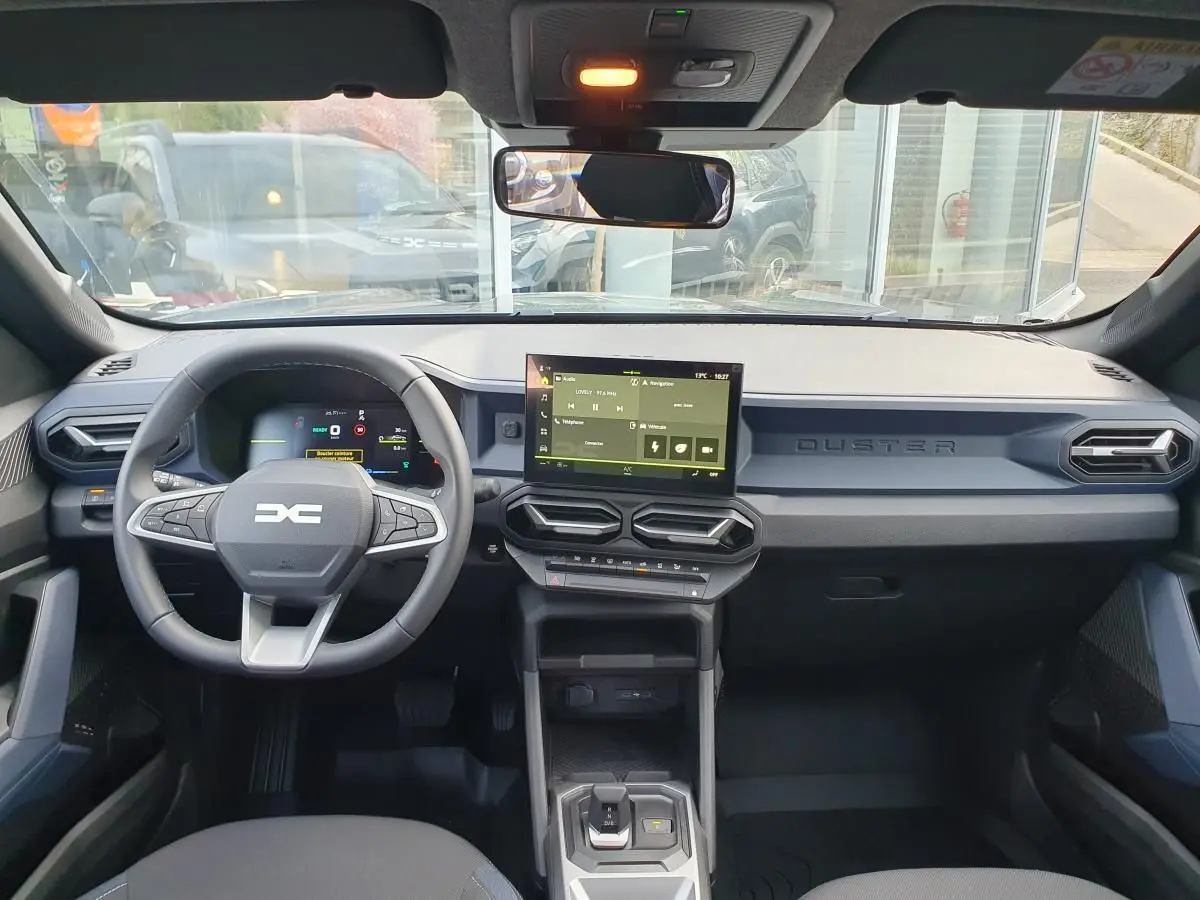 Vue intérieure avant du Dacia Duster 1.6 Hybrid 140 gris schiste, tableau de bord moderne avec écran tactile central.